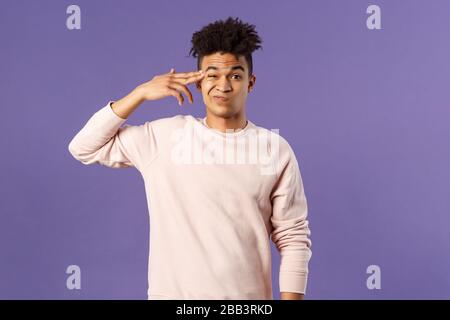 Porträt des jungen Teenagers, hispanischer männlicher Student verliert seinen Verstand zu Hause abschrecken, zeigt auf Tempel mit Fingerpistole und grimacing als Schießen Stockfoto