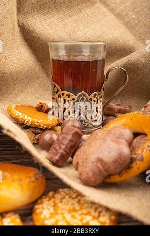 Ein facettiertes Glas Tee in einem Vintage-Cup-Halter, Bagels, Plätzchen, Schokoladenkuchen und Schokolade auf einem Hintergrund aus rauher Struktur. Nahaufnahme Stockfoto