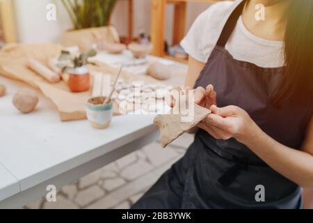 Aus der Nähe von Frauenhänden sculpt sie vor dem Hintergrund eines Tisches in einem Tonstudio aus Ton Stockfoto