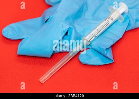 Weißes 2-ml-Spritzenmakro auf roter Oberfläche, blauer Gummihandschuh. Medizinliches Injektions-, Impfstoff- und Heilmittel Stockfoto