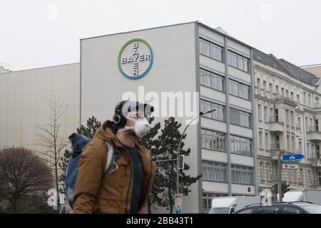 Berlin, Deutschland. März 2020. Micha geht mit einer Gesichtsmaske an einem Logo des Chemiekonzerns Bayer vorbei. Die Bayer AG will den Kampf gegen die Coronavirus-Pandemie mit weiteren Maßnahmen unterstützen und stellt bundesweit Geräte aus Forschungsabteilungen zur Verfügung. Allein am Standort Berlin-Wedding arbeiten mehr als 140 Mitarbeiter ehrenamtlich in einem neuen Prüflabor. Kredit: Jörg Carstensen / dpa / Alamy Live News Stockfoto
