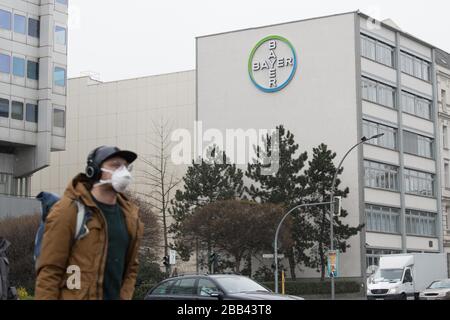 Berlin, Deutschland. März 2020. Micha geht mit einer Gesichtsmaske an einem Logo des Chemiekonzerns Bayer vorbei. Die Bayer AG will den Kampf gegen die Coronavirus-Pandemie mit weiteren Maßnahmen unterstützen und stellt bundesweit Geräte aus Forschungsabteilungen zur Verfügung. Allein am Standort Berlin-Wedding arbeiten mehr als 140 Mitarbeiter ehrenamtlich in einem neuen Prüflabor. Kredit: Jörg Carstensen / dpa / Alamy Live News Stockfoto