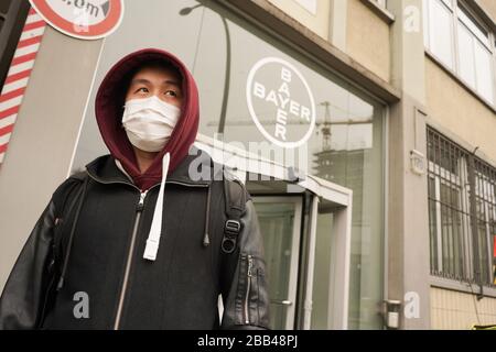 Berlin, Deutschland. März 2020. Ein Mann mit Gesichtsmaske läuft an einem Logo des Bayer-Chemieunternehmens vorbei. Die Bayer AG will den Kampf gegen die Coronavirus-Pandemie mit weiteren Maßnahmen unterstützen und stellt bundesweit Geräte aus Forschungsabteilungen zur Verfügung. Allein am Standort Berlin-Wedding arbeiten mehr als 140 Mitarbeiter ehrenamtlich in einem neuen Prüflabor. Kredit: Jörg Carstensen / dpa / Alamy Live News Stockfoto
