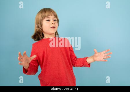 Süßer europäischer Junge in rotem Pullover, der auf isoliertem blauem Studiohintergrund posiert. Stockfoto