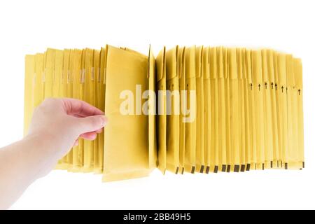 Weibliche Hand, die einen gepolsterten Umschlag aus dem Haufen zieht. Draufsicht, isoliert auf weiß. Stockfoto