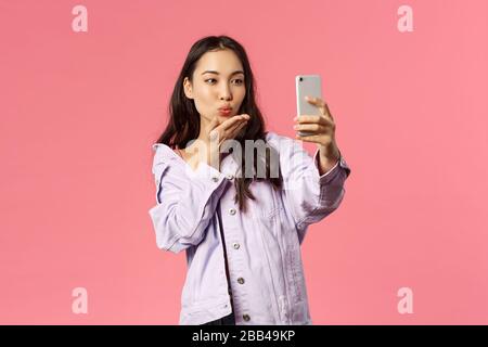 Online-Lifestyle, Menschen und Beauty-Konzept. Schönes modernes und stilvolles asiatisches Mädchen, Internet-Blogger, die Küsse per Telefonkamera schicken, selfie oder nehmen Stockfoto