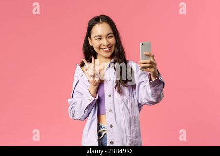 Online-Lifestyle, Menschen und Beauty-Konzept. Stilvolles, hübsches koreanisches Mädchen, das mit einem Freund im Online-Videochat spricht, verwirrt und selfie mit einem Foto mitnimmt Stockfoto