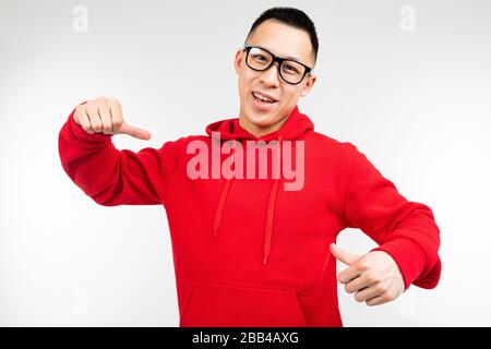 Schöner brunette-asiat in rotem Pullover und Brille für Augenlicht zeigt Finger auf einem Pullover auf weißem Hintergrund. Stockfoto
