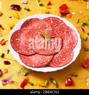 Nahaufnahme einiger Scheiben von veggie Salami in einem Teller, auf einer goldfarbenen strukturierten Oberfläche Stockfoto