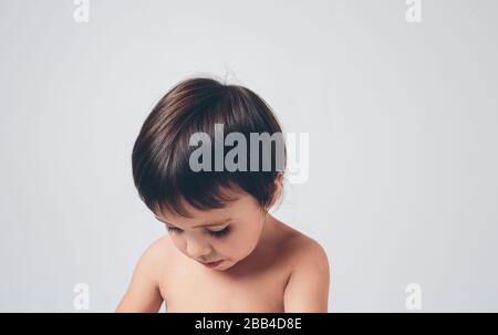 Trauriges, desorientiertes Kind blickt auf einen weißen Hintergrund. Die Kieme oder der Junge hat braune Haare und Haut Stockfoto