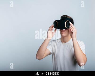 Freudiger junger Mann mit VR-Headset für virtuelle Realität. Stehen Sie allein im Raum und isoliert auf weißem Hintergrund. Realistisches Video. Stockfoto