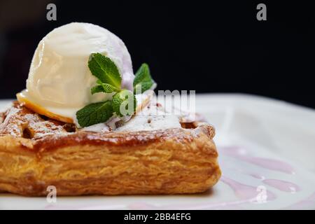 Nahaufnahme von einem Stück Krustenkuchen mit weißer Vanilleeis auf der Oberseite. Köstliches Dessert mit frischer Minze und Puderzucker auf weißem Teller im Restaurant. Stockfoto