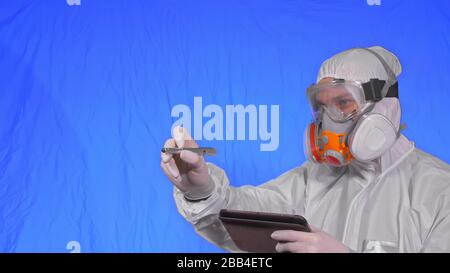 Wissenschaftler Virologe in Atemschutzgeräten schreibt in einem Tablet-Computer mit Eingabestift. Mann, der eine medizinische Schutzmaske trägt. Chroma Key blau. Stockfoto