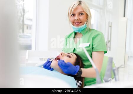 Porträt eines Zahnarztes mit Bohrer und einem Zahnspiegel in den Händen, der einer hübschen Patientin die Zähne behandelt Stockfoto