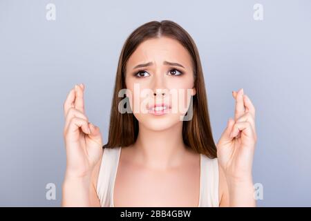 Die junge süße Dame hält die Finger über den Daumen und schaut nach oben, in der Hoffnung auf viel Glück, bevor sie zu einem Bewerbungsgespräch oder einer Prüfung auf reinem Hintergrund geht Stockfoto