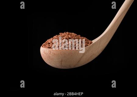 Roter Reis in Holzlöffel auf schwarzem Grund . Nahaufnahme Stockfoto