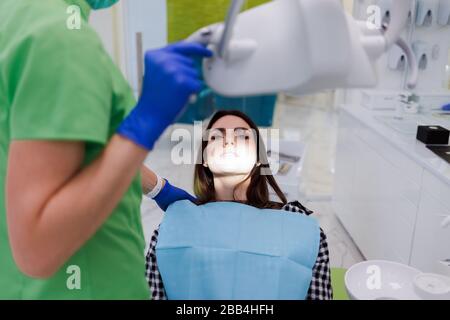 Das Mädchen liegt auf einem Stuhl bei der Verabredung des Zahnarztes. Der Zahnarztarzt setzt eine Lampe auf die Zähne des Patienten Stockfoto