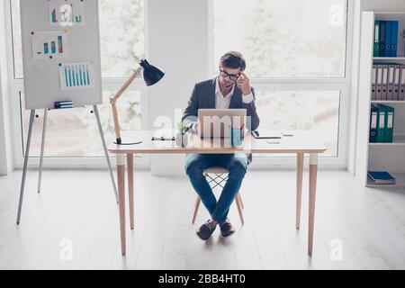 Die ganze Größe eines jungen, nachdenklichen Geschäftsmannes, der im Büro an einem Laptop arbeitet. Er denkt an neue Ideen für den Start Stockfoto