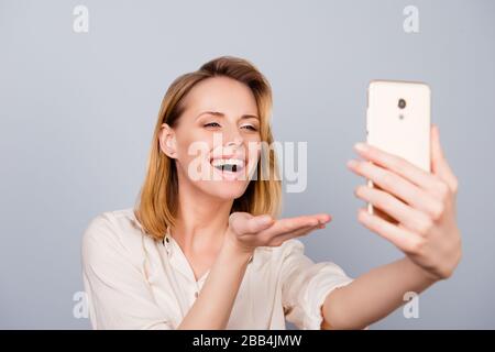 Küssen Sie sich! Die junge romantische blonde Dame schickt ihrem Freund den Luftkuss in die Kamera, während sie einen Videoanruf auf rein grauen Hintergrund hat Stockfoto