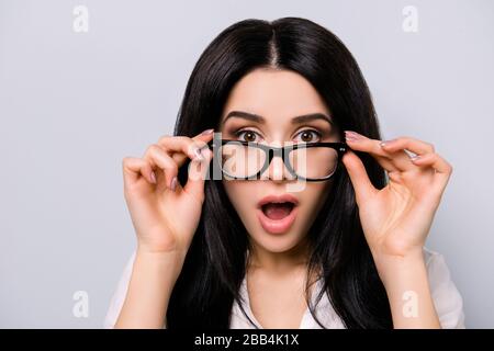 Keine Möglichkeit! Wirklich?! Schockiert brünette hübsches Mädchen in einer Brille hält sie mit den Fingern. Sie ist aufgeregt und mit offenem Mund auf reinem grauen Hintergrund Stockfoto