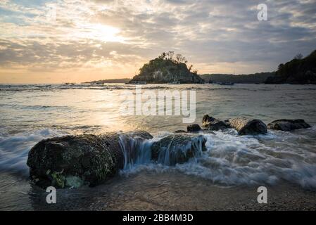 Crystal Bay bei Ebbe mit dem Sonnenuntergang durch die Felsinsel strömende Meerwasser über Felsen und Pfütze in Nusa Penida, Bali, Indonesien Stockfoto