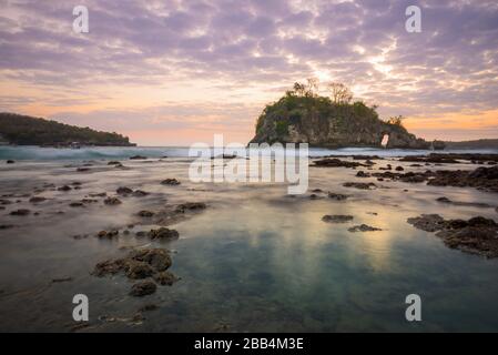 Crystal Bay bei Ebbe mit dem Sonnenuntergang durch die Felsinsel strömende Meerwasser über Felsen und Pfütze in Nusa Penida, Bali, Indonesien Stockfoto
