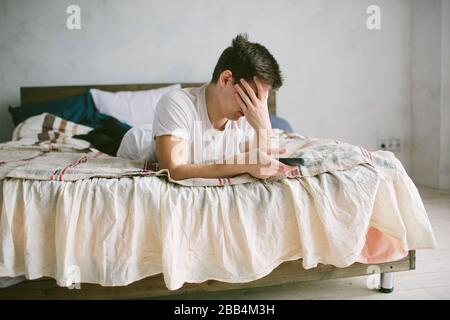 Kerl, der die Fernbedienung verwendet, während er zu Hause auf dem Bett sitzt. Fröhlicher attraktiver junger Mann beim Fernsehen. Menschliche Emotionen im Gesicht. Stockfoto