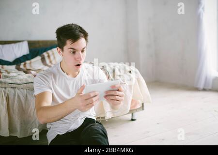 Gutaussehender Mann, der auf Tablet surft. Kerl im Gespräch mit Freunden, Videokonferenz, Skype, Tablet. Der junge Student scrollt soziale Netzwerke Stockfoto