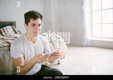 Gutaussehender Mann, der auf Tablet surft. Kerl im Gespräch mit Freunden, Videokonferenz, Skype, Tablet. Der junge Student scrollt soziale Netzwerke. Stockfoto