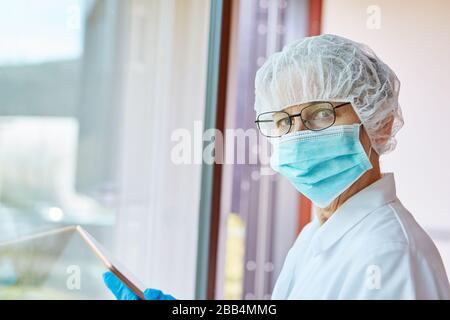 Der weibliche Arzt mit Gesichtsmaske in der Klinik betrachtet das Röntgenbild der Covid-19-Patientin auf dem Tabletcomputer während der Coronavirus-Epidemie Stockfoto