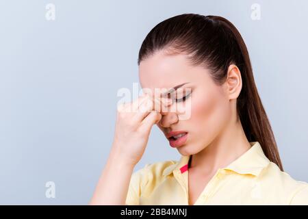 Schlechter Tag. Überarbeiteter gestresster junger Brunette-Lady hat Kopfschmerzen und kämpft. Sie trägt gelbes T-Shirt und steht auf hellem Hintergrund Stockfoto