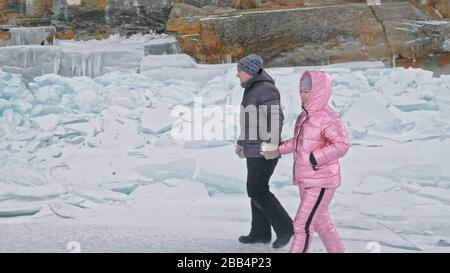 Das Paar hat Spaß beim Winterspaziergang vor dem Eis des zugefrorenen Sees. Liebhaber liegen auf klarem Eis, haben Spaß, küssen und umarmen sich. Ansicht von oben. Stockfoto
