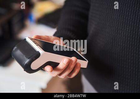 Bankterminal für kontaktlose Zahlung. Der junge Mann hält ein Terminal in seinen Händen Stockfoto