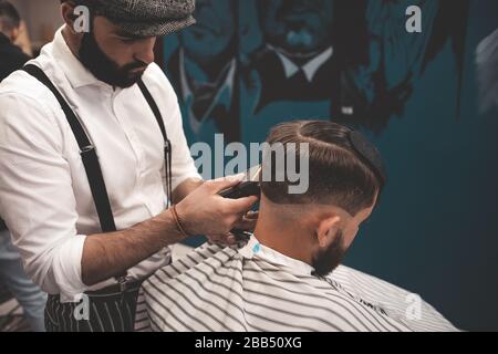 Barbier Mann rasiert Kunden in Barbershop. Stylischer Friseur macht Haarschnitt für Kerl Stockfoto