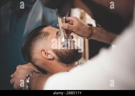 Barbier macht einen Bart Schnitt für einen Kunden. Hipster Kunde besuchte Barbershop Stockfoto