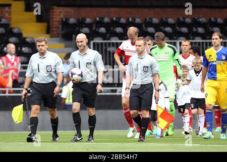 Spielbeamte führen beide Teams vor dem Anpfiff auf das Spielfeld Stockfoto