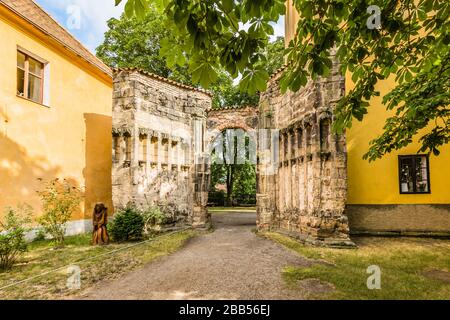 Panensky Tynec, Tschechien - 15. Juli 2019: Steinernes Tor der unvollendeten gotischen Marienkirche aus dem 14. Jahrhundert. Gelbe Gebäude. Stockfoto