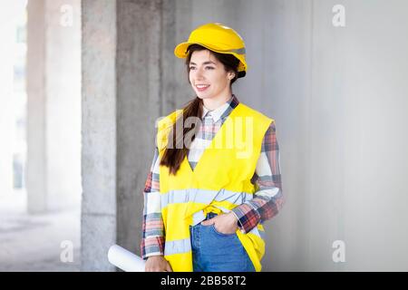 Porträt einer lächelnden jungen Baumeisterin mit Zeichnungen in der Hand Stockfoto