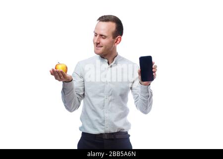 Kaukasischer männlicher Geschäftsmann, der ein Handy in Schwarz hält und einen rot-gelben apfel hält. Er trägt ein Hemd. Emotionales Porträt. Isoliert auf Whit Stockfoto