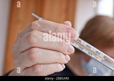 Medizinisches Thermometer zur Messung der Körpertemperatur in der Hand im Vordergrund, der Hintergrund ist verschwommen. Eine Frau hält ein Thermometer in der Hand. Stockfoto