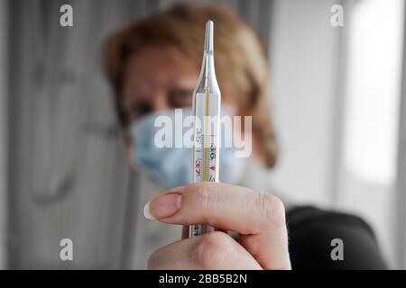 Medizinisches Thermometer zur Messung der Körpertemperatur in der Hand im Vordergrund, der Hintergrund ist verschwommen. Eine Frau hält ein Thermometer in der Hand. Stockfoto