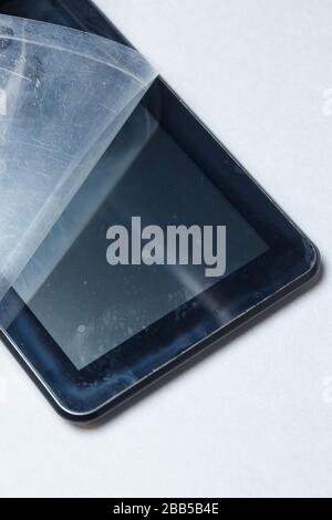 Schwarz verkratztes Tablett mit einer Schutzfolie auf grauem Hintergrund. Schützen Sie den Bildschirm Ihres Geräts Stockfoto