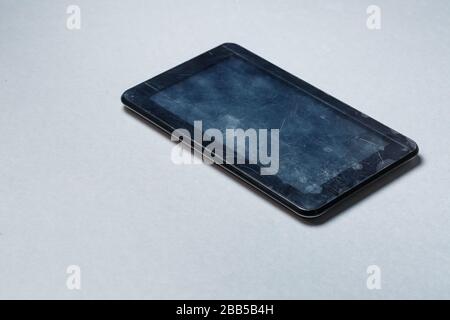 Schwarz verkratztes Tablett mit einer Schutzfolie auf grauem Hintergrund. Schützen Sie den Bildschirm Ihres Geräts Stockfoto