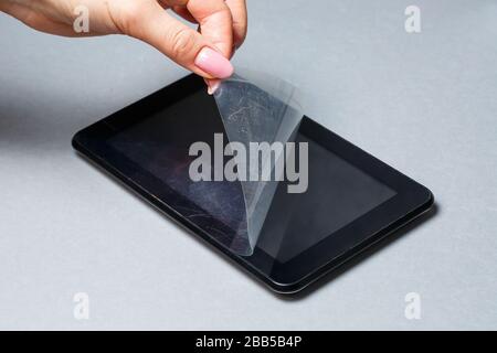 Schwarz verkratztes Tablett mit einer Schutzfolie auf grauem Hintergrund. Schützen Sie den Bildschirm Ihres Geräts Stockfoto