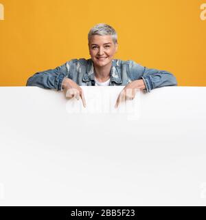 Freier Platz Für Werbung. Frau mittleren Alters lehnt sich an leeres weißes Brett Stockfoto