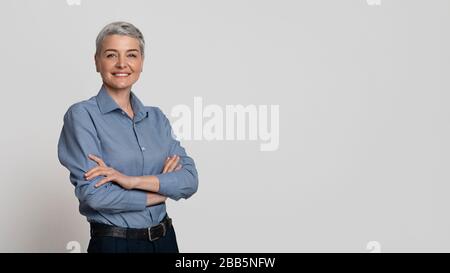 Porträt Einer Reifen Geschäftsfrau, Die Mit Gefalteten Armen Über Hellem Hintergrund Posiert Stockfoto
