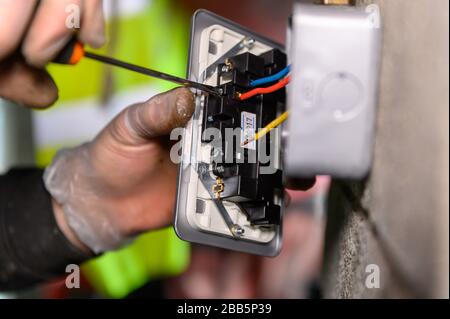 Steckernhänder verkabeln einen UK-Steckdosenstecker an der Garagenwand mit Schraubendreher Stockfoto