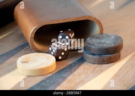 Braune Backgammon-Würfel und -Stücke auf Holzbrett Stockfoto