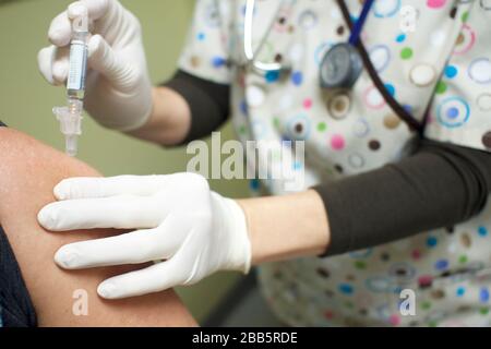 Krankenschwester, die dem Patienten einen Impfstoff im Bizeps gibt. Handschaufel mit Handschuhen, chirurgische Peelings, die dem Patienten eine hypodermische Nadel injizieren. Covid-19, Coronavirus-Schutz. Stockfoto