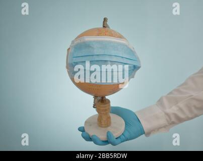 Global Pandemic Covid-19 Coronavirus, Arm des Arztes, der den Globus mit blauer Operationsmaske hält. Studio Shot, ausgestreckter Arm mit Labormantel, Handschuhen Stockfoto